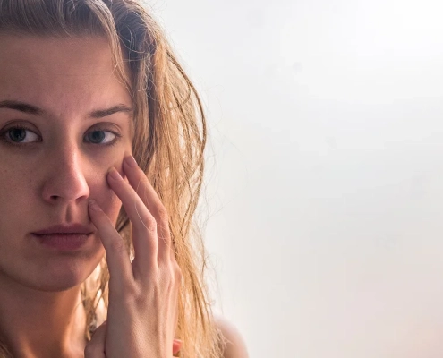 Une femme se regarde dans le miroir, examinant son visage avec une expression préoccupée.