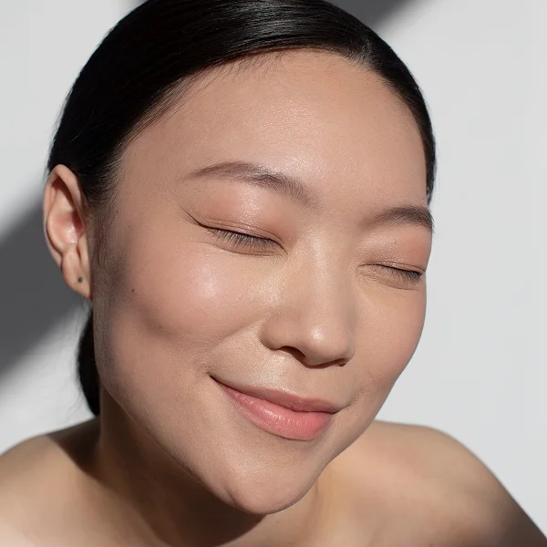 Femme souriante les yeux fermés, exprimant la joie et la sérénité, avec un teint terne.