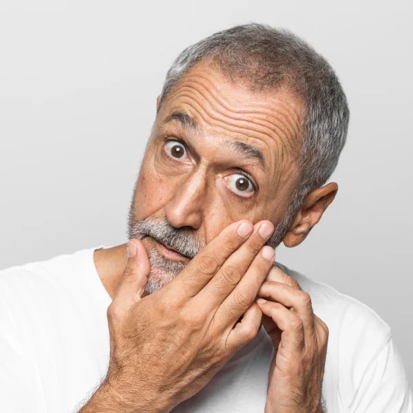 Un homme barbu en chemise blanche examine son visage, illustrant un traitement de rajeunissement du visage.