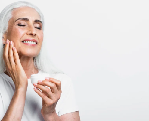 Une femme âgée aux cheveux blancs applique une crème sur son visage, mettant en avant les bienfaits essentiels du collagène.