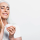 Une femme âgée aux cheveux blancs applique une crème sur son visage, mettant en avant les bienfaits essentiels du collagène.